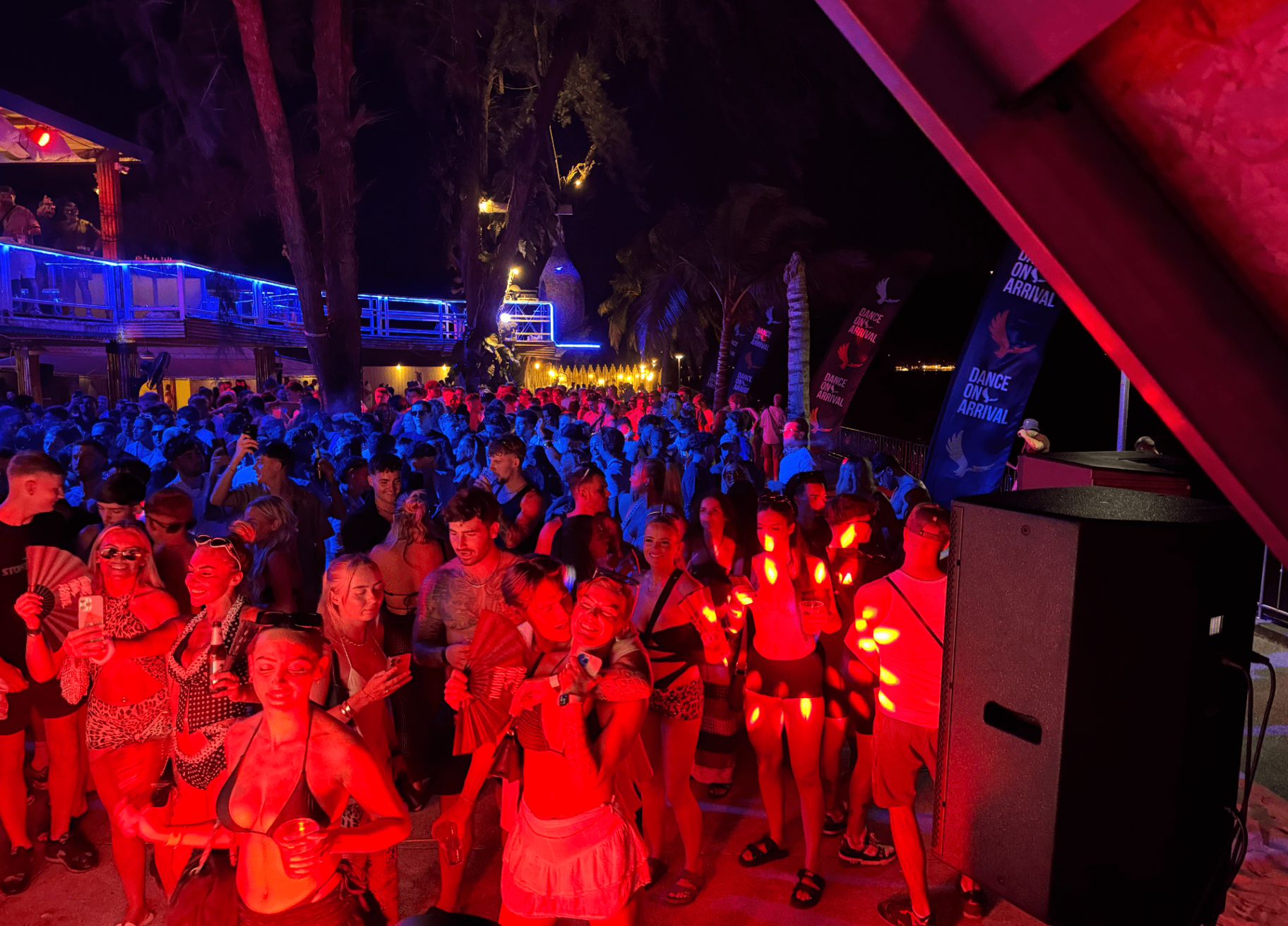 Packed beach club crowd at night with stage lighting and sound system in Phuket